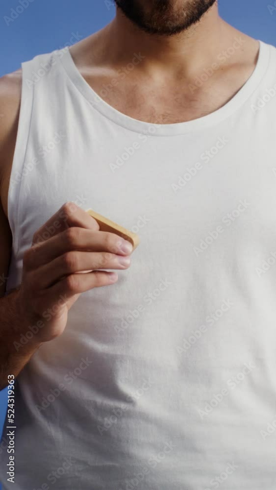A young man makes a face lifting massage with a roller massager, vertical video on studio background