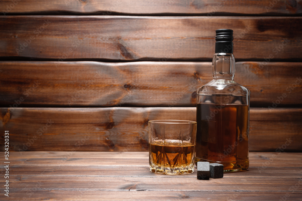 Whiskey in the drinking glass and bottle on the brown wooden table background with copy space. Whiskey in the drinking glass and bottle on the brown wooden table background with copy space.