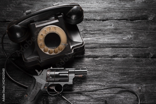 Old retro rotary phone and black gun on the wooden detective agent desk table background concept.