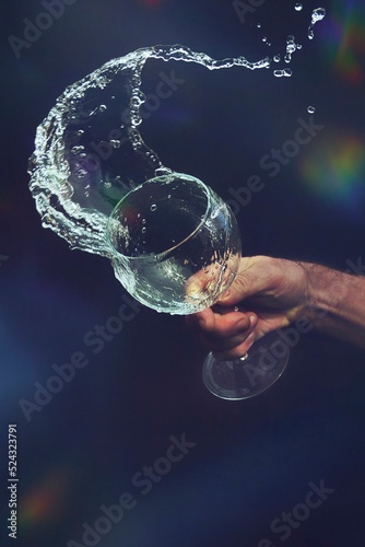 Una mano derramando el agua de una copa de cristal, cuyo movimiento queda congelado en el aire. photo