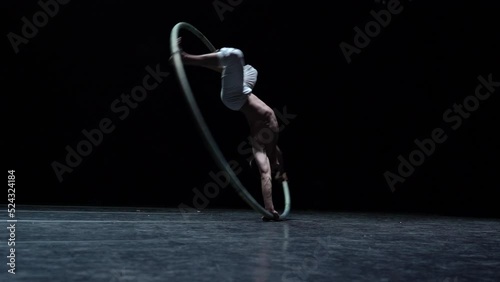 Muscular circus artist perform Cyr Wheel on a black background. Concept of willpower, motivation and healthy lifestyle