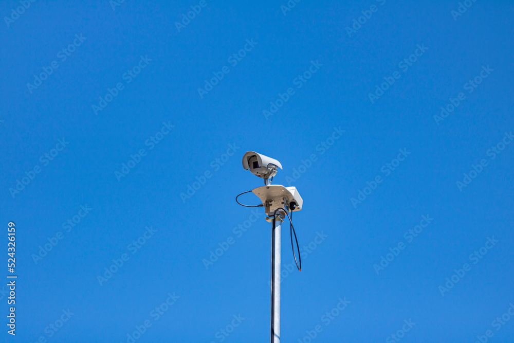 A CCTV security camera on top of a light pole with blue sky behind it