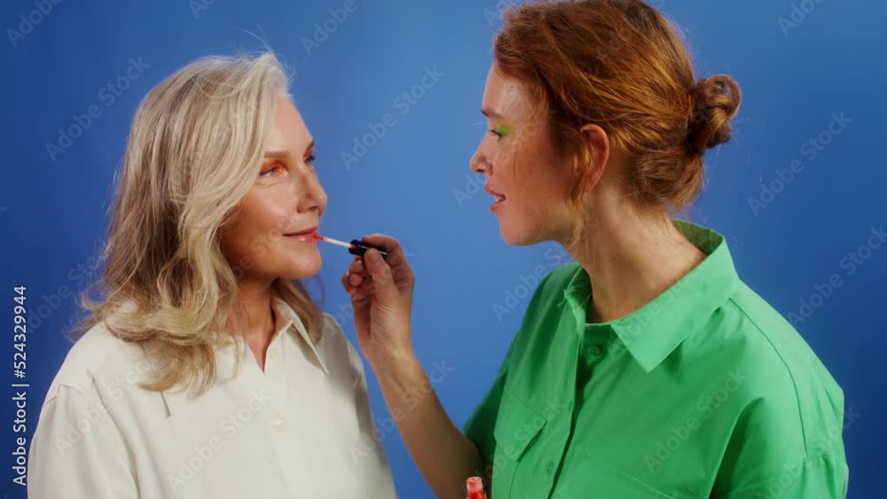 Young woman paints her elderly friend's lips, monochrome background, Young woman paints her elderly friend's lips, monochrome background,