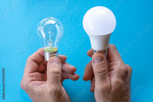 An incandescent lamp and an energy-saving lamp in hands on a blue background. Energy saving concept