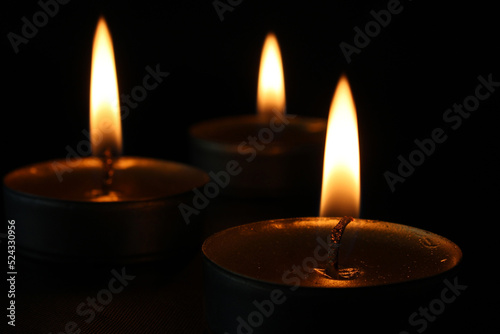 Three burning candles close-up on a black background with copy space. Blurred background