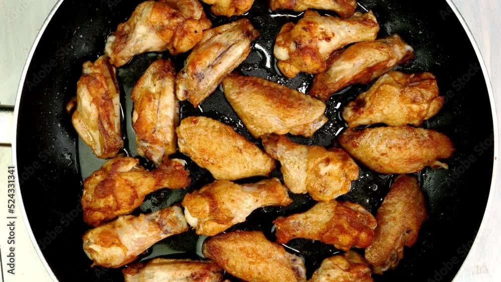 Many crispy fried chicken wings pieces in frying pan turning slowly on turntable. Many crispy fried chicken wings pieces in frying pan turning slowly on turntable.