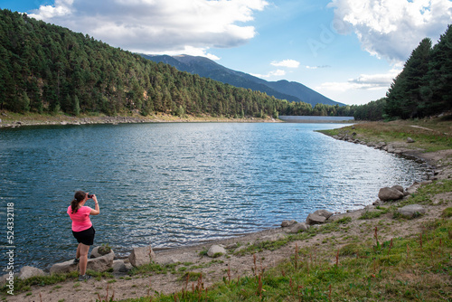 Young girl photographing a lake between mountains