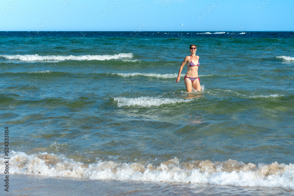 Attractive sporty short haired woman in her thirties, wearing bikini, standing in the blue sea with her arms spread on a sunny summer day. Concept for holiday, vacation, relaxation, mental health,joy. Attractive sporty short haired woman in her thirties, wearing bikini, standing in the blue sea with her arms spread on a sunny summer day. Concept for holiday, vacation, relaxation, mental health,joy.
