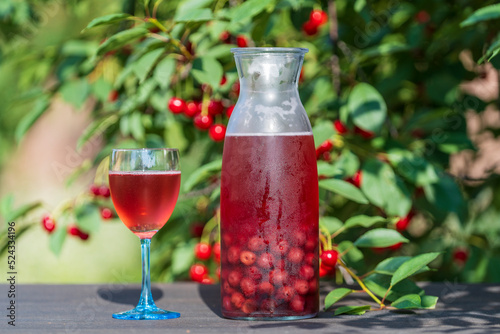 Homemade cherry brandy in a glass and in a glass bottle on a wooden table in a summer garden