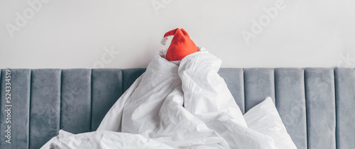  Wake up morning after party holidays. Woman in Santa hat under blanket in bed.