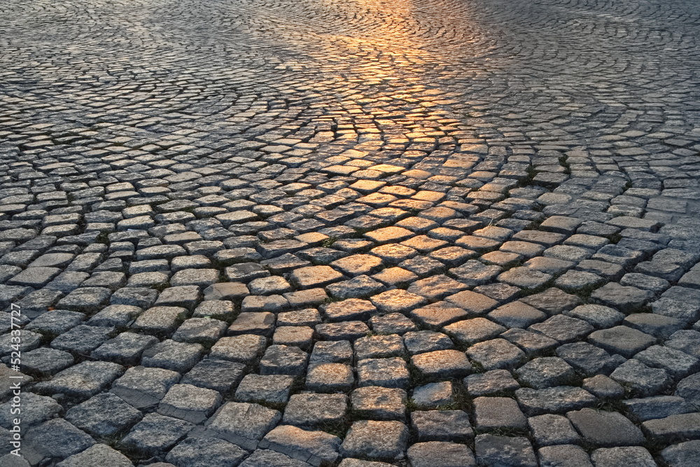 A street in the old town made of granite cubes illuminated by the setting sun - obrazy, fototapety, plakaty 