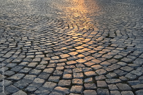 Fotografia A street in the old town made of granite cubes illuminated by the setting sun