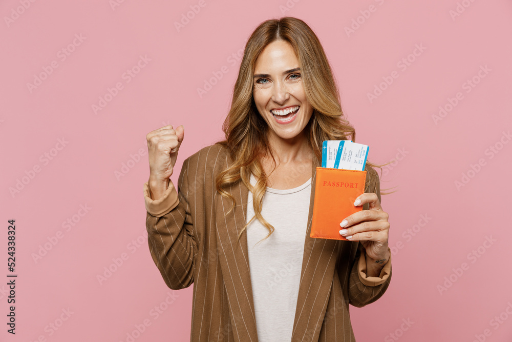 Traveler tourist woman wear jacket hold passport boarding tickets do winner gesture isolated on plain pastel light pink background. Passenger travel abroad weekends getaway Air flight journey concept. Traveler tourist woman wear jacket hold passport boarding tickets do winner gesture isolated on plain pastel light pink background. Passenger travel abroad weekends getaway Air flight journey concept.