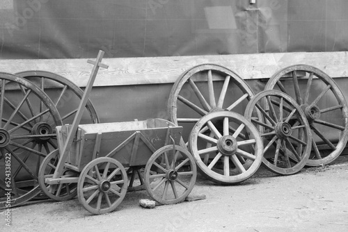 Obraz na plátne An old handcart and old wooden horse cart wheels leaning against the wall