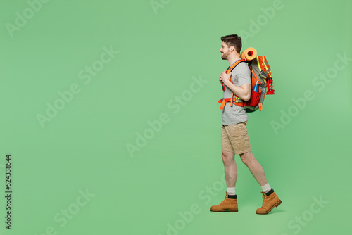 Full body side view young mountaineer traveler white man carry backpack stuff mat walk isolated on plain green background. Tourist leads active healthy lifestyle. Hiking trek rest travel trip concept.