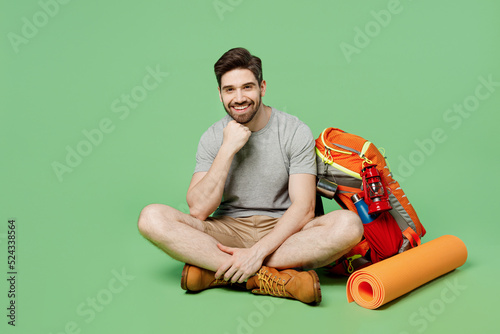 Full body young traveler white man near backpack stuff mat sit take break look camera isolated on plain green background Tourist lead active healthy lifestyle Hiking trek rest travel trip concept. #524338564
