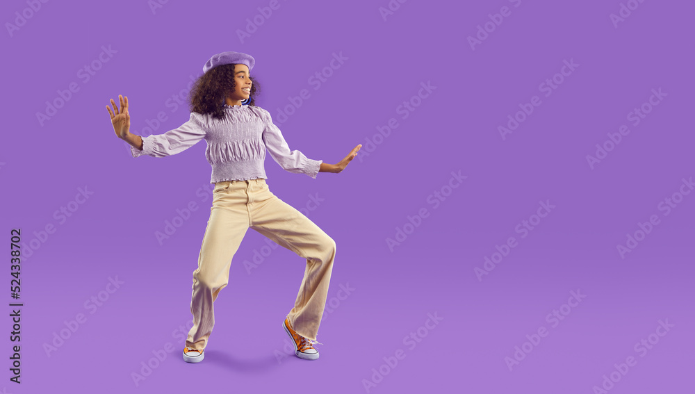 Narrow shot of overjoyed teen African American girl in casual clothes have fun dancing on purple studio background. Happy biracial teenager make funny dancer moves. Copy space.