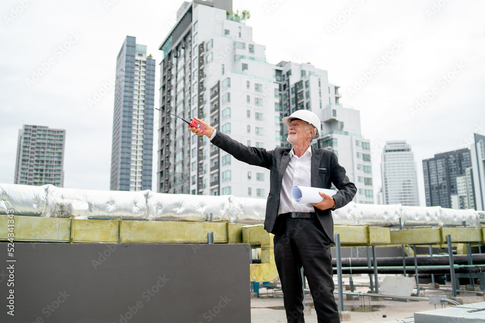 Senior man as professional engineer or technician use walkie talkie point over and stand near line of air vents on rooftop of construction site. Senior man as professional engineer or technician use walkie talkie point over and stand near line of air vents on rooftop of construction site.
