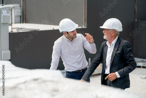 High view of two engineer or technician workers discuss together on rooftop of constuction site.