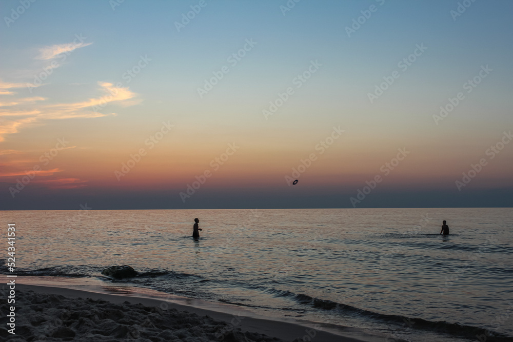 Beautiful sunset on the Polish beach in Międzywodzie. In the sea you can see two children playing. 10 August 2020