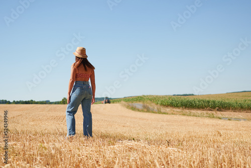 A beautiful young woman standing in a wheat field on a sunny day in a countryside © Érik Glez.