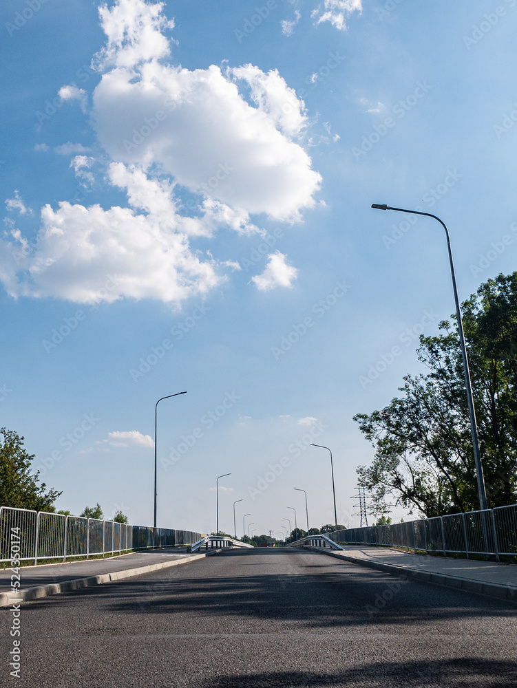 droga idąca przez most osłonięta barierkami i kratką w porze letniej, błękitne niebo, z prawie bezchmurną pogodą - obrazy, fototapety, plakaty 