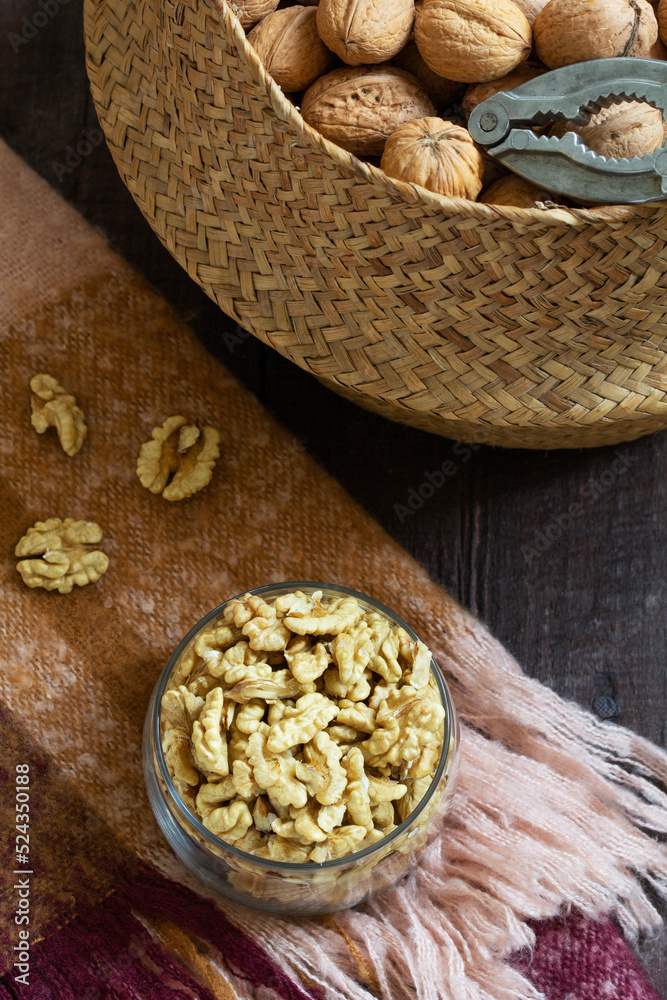 Whole walnuts and a nutcracker in a basket, nut kernels in a jar on a wooden table.