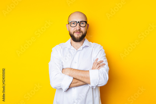 Man bald with a beard in glasses in a white shirt on a yellow background