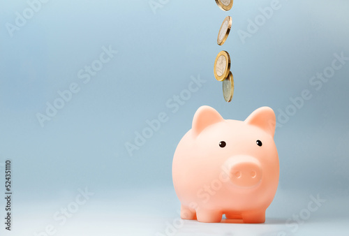 Pink piggy bank with falling coins on blue background photo