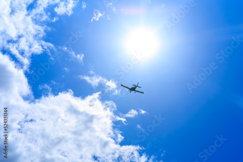The plane is flying in a blue sky among clouds and sunlight
