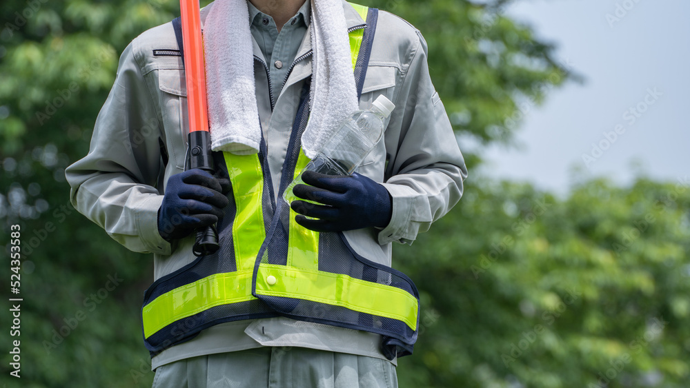 プラスチックボトルの水を持つ警備員の男性|建設業・警備業の熱中症対策イメージ プラスチックボトルの水を持つ警備員の男性|建設業・警備業の熱中症対策イメージ