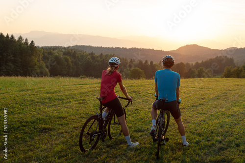 Woman and man, road racing bikers, sitting on bicycles, enjoying a beautiful mountain landscape at sunset