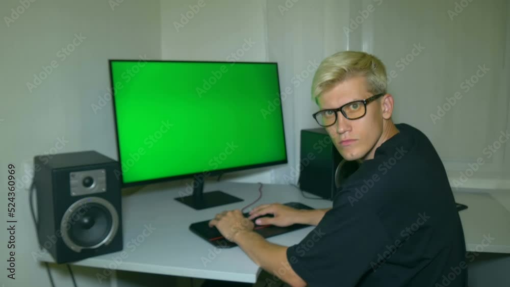 Chroma key on the screen of computer. Man is typing text on green computer screen and turns to the camera and looks neutral.