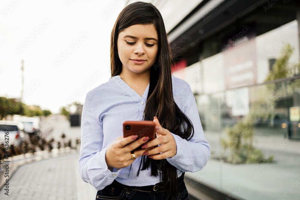 Young businesswoman using smartphone in downtown streets near business buildings Young businesswoman using smartphone in downtown streets near business buildings