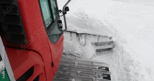 Snowcat ratrack with snowplow preparing the ski slope, driving through the deep snow piste in the ski resort. Heavy machinery transport free style skiers on mountain peak photo