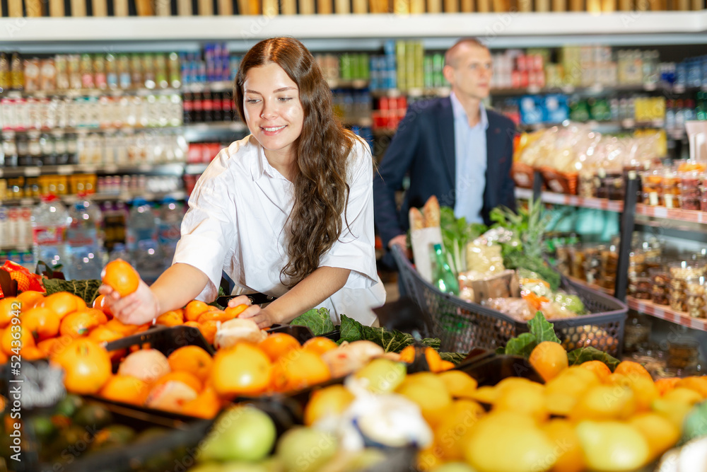Female shopper picks ripe oranges on grocery store shelves