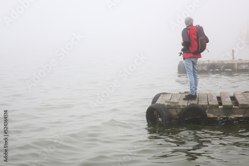 Hiker with red jacket and backpack in dock with mist