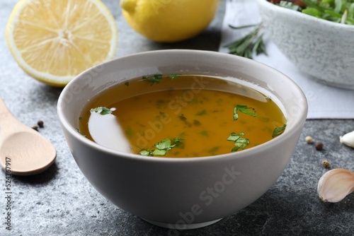 Bowl with lemon sauce on grey table, closeup. Delicious salad dressing