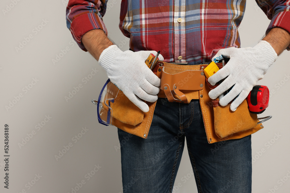 Professional builder with tool belt on light background, closeup Professional builder with tool belt on light background, closeup