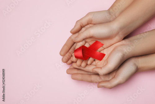 Woman and girl holding red ribbon on pink background, top view with space for text. AIDS disease awareness