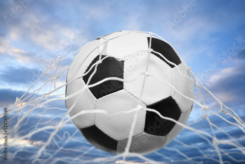 Soccer ball in net against cloudy sky