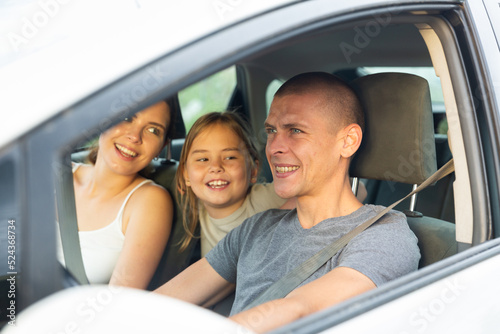 Positive young adult man driving car during trip with his family, woman and little girl © JackF