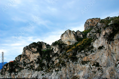 Wonderful scene in Amalfi coast with a spiky mountain ridge and some terracing, technological towers, a red and white building perching on the left side and a hazy dreamy azure sky on a summer day
