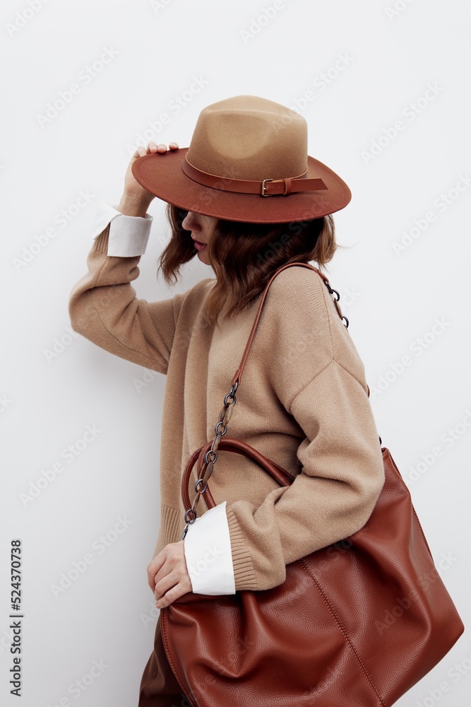 a sweet beautiful woman stands on a white background in a sweater, shirt and hat, put a bag on one shoulder, put her hand on it, turned her head to the side, covering her face with a hat a sweet beautiful woman stands on a white background in a sweater, shirt and hat, put a bag on one shoulder, put her hand on it, turned her head to the side, covering her face with a hat