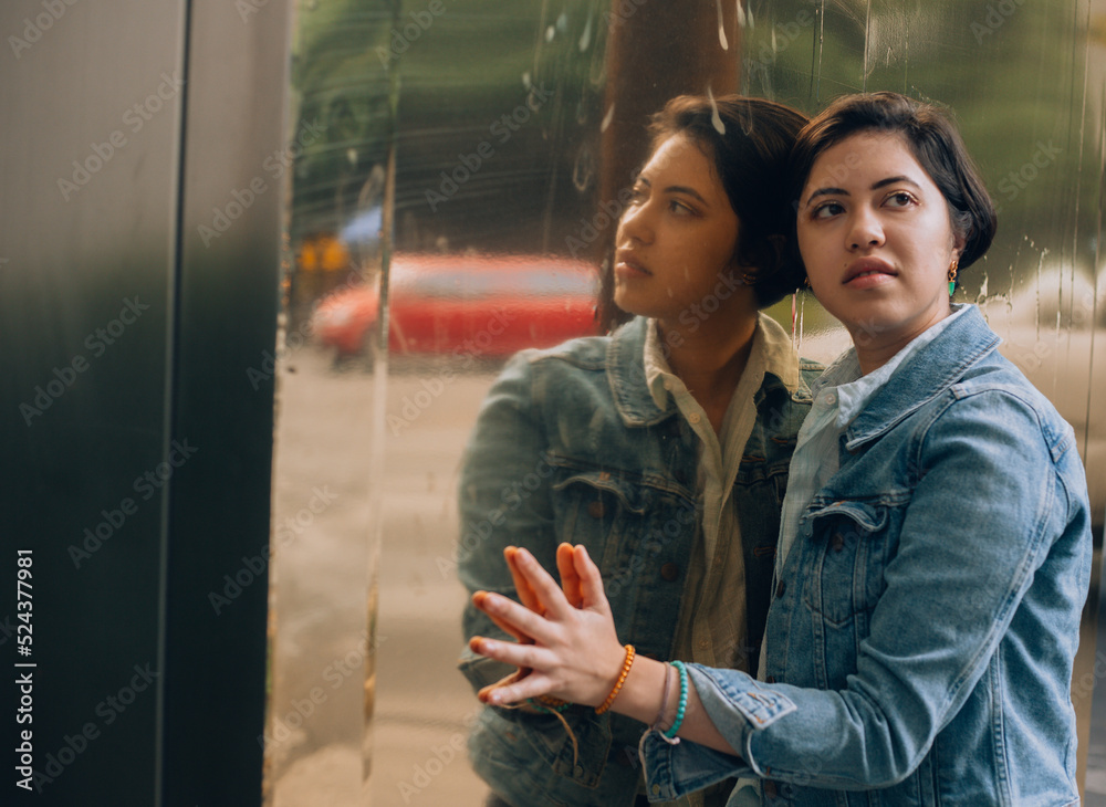 Naklejka premium Pretty and cheerful young generation z girl with short hair dressed in blue with a denim jacket, sunglasses and gold jewelry posing in front of a reflective surface with a slight gold color.