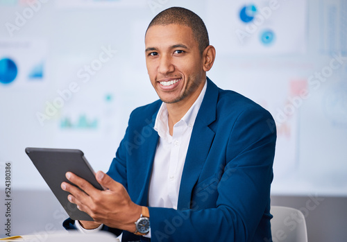 Successful financial businessman smiling while browsing on a digital tablet in the office. Portrait of a male professional accountant feeling positive after completing a deal or finishing a work task