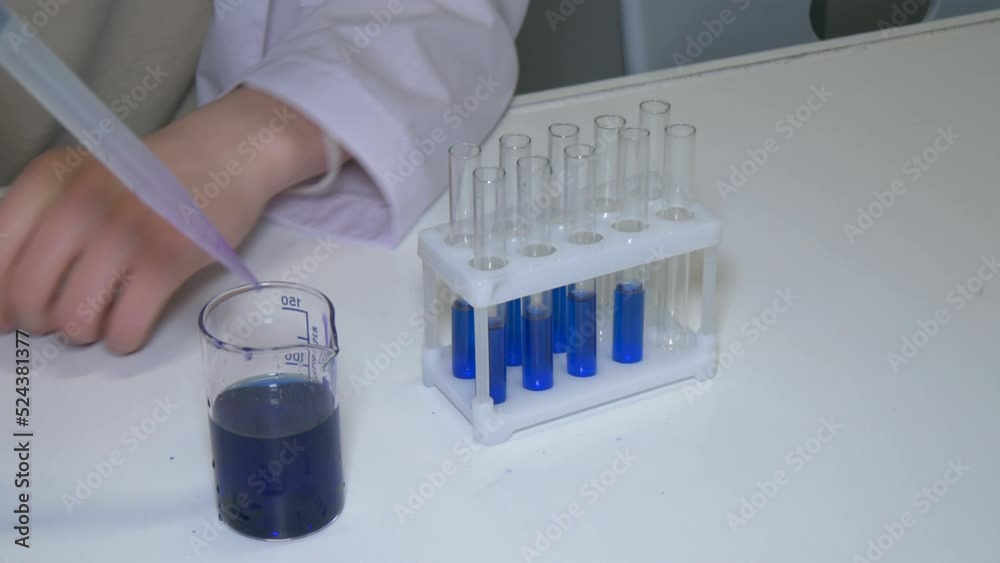 Scientist in a laboratory. Laboratory assistant pours blue liquid from container into test tubes. Scientist in a laboratory. Laboratory assistant pours blue liquid from container into test tubes.