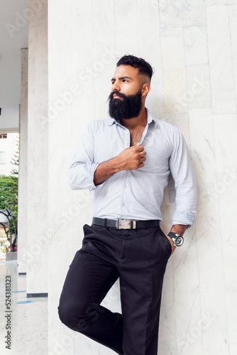 Caucasian handsome man with fashionable stylish long beard, male business person posing at white wall of building outdoors