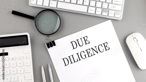 DUE DILIGENCE written on paper with office tools and keyboard on the grey background