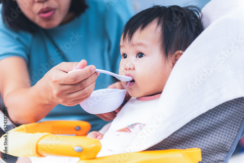 9 month old baby girl Eating baby food which her mother is feeding, to people and food development for baby newborn and infant concept.